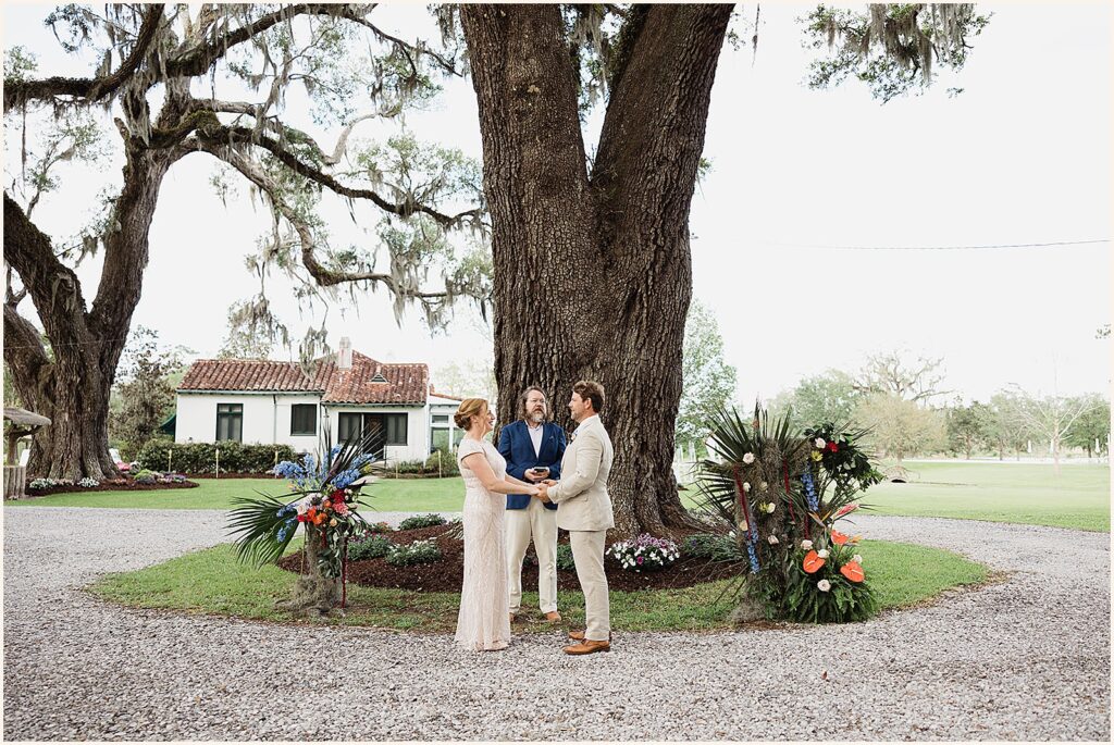 A bride and groom hold hands beneath an oak tree during a backyard wedding in New Orleans.