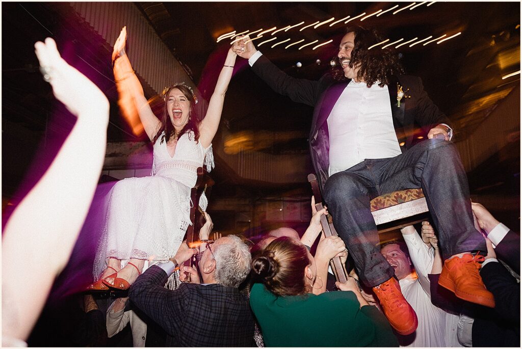 Wedding guests lift up a bride and groom for the hora.