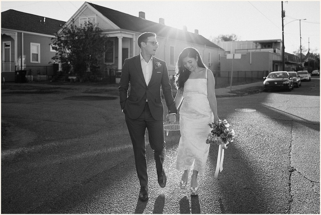 A bride and groom hold hands as they walk down a New Orleans street.