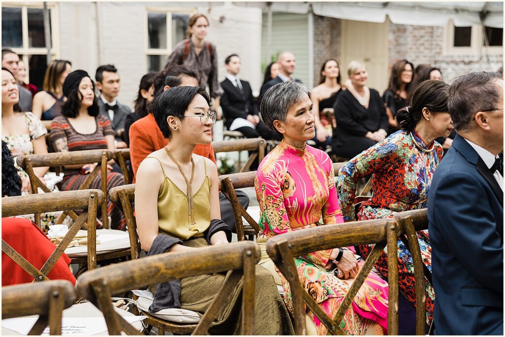 Two women in colorful clothes watch a wedding ceremony.