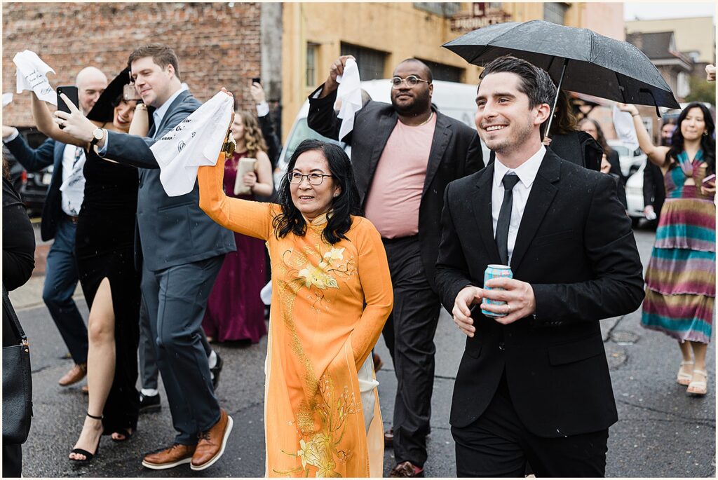Wedding guests wave handkerchiefs as they walk.