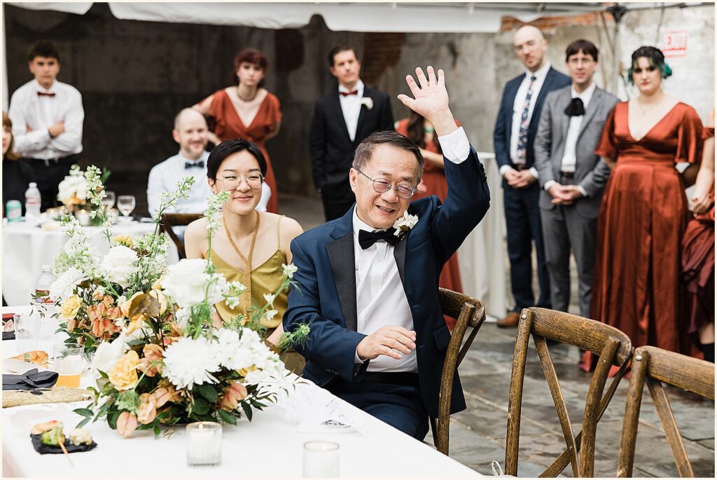 A father waves from a reception table.