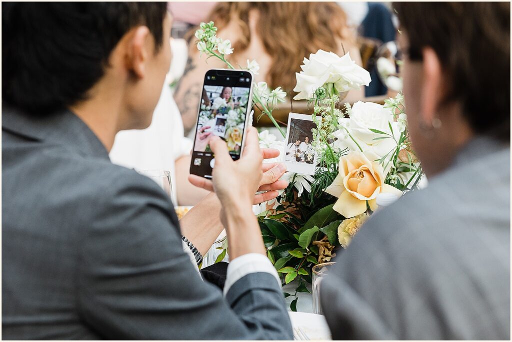 A wedding guest takes a phone photo of an instax photo.