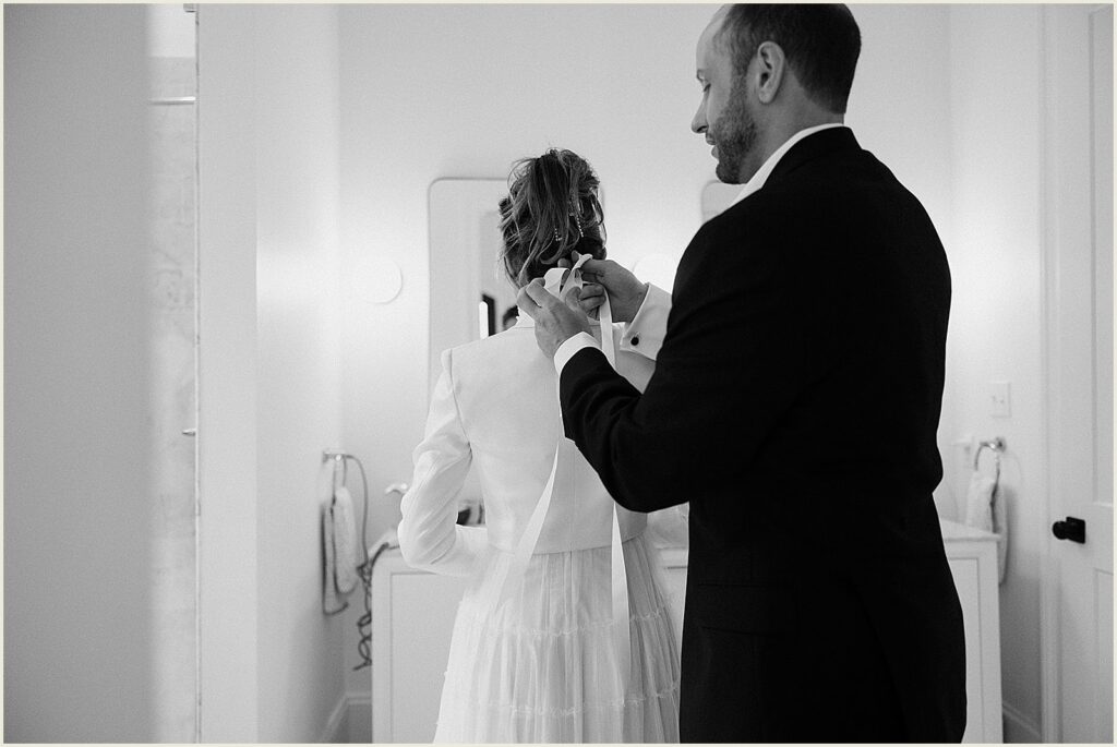 A groom helps fasten a bride's wedding dress before their New Orleans wedding.