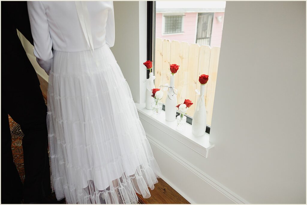 A bride walks past a window with roses in vases.