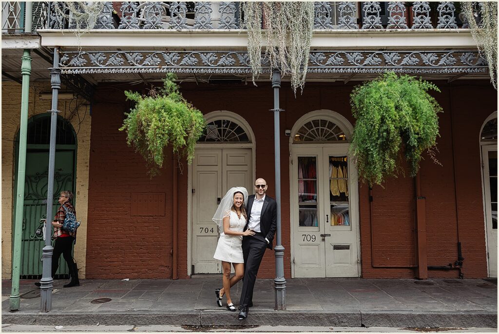 A bride and groom lean against a balcony post in front of a French Quarter building on the day they elope in New Orleans.
