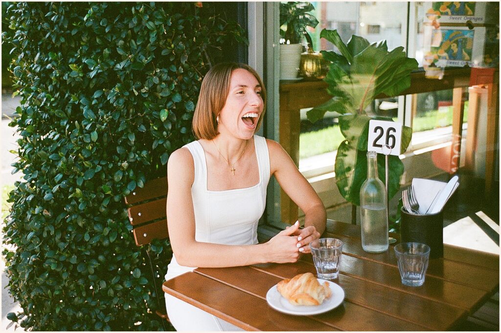A woman in a white dress laughs in a film engagement photo.