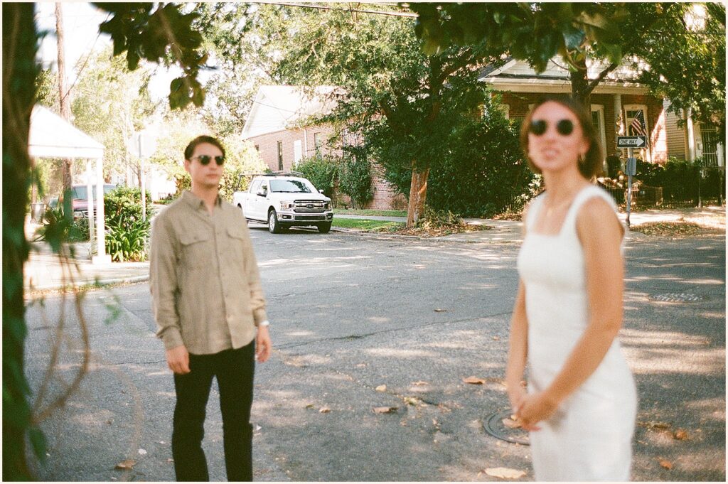 A man and woman in sunglasses pose for a New Orleans engagement photographer in a Garden District street.