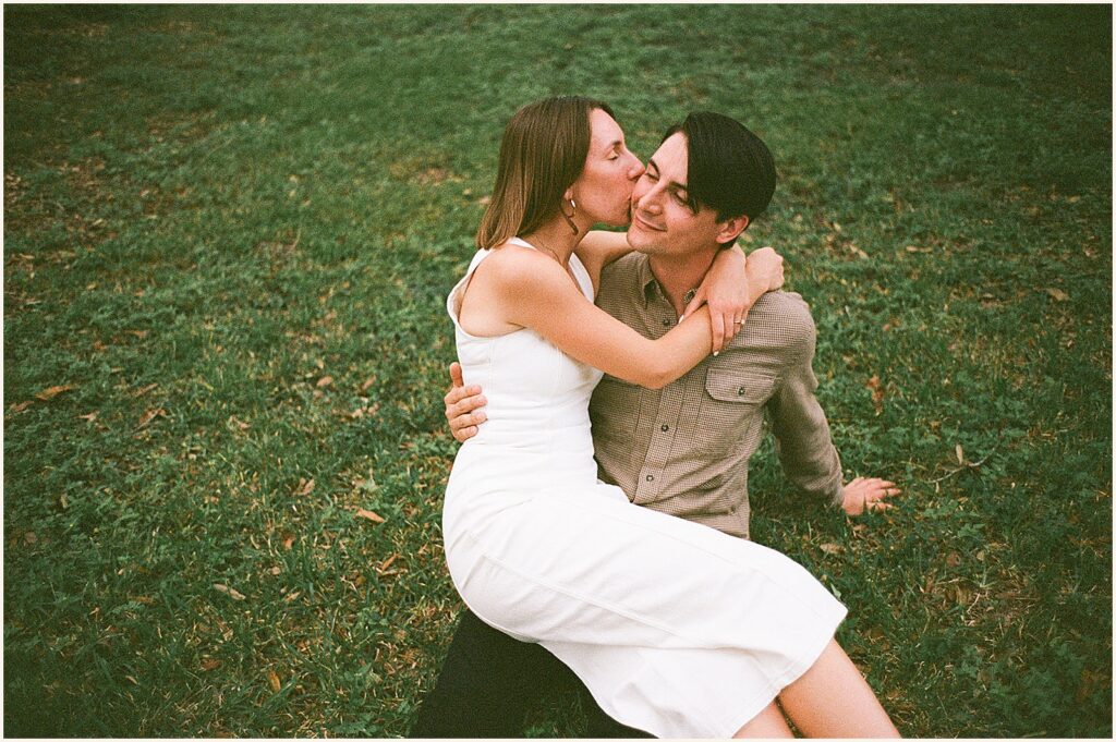 A woman kisses a man's cheek in a film engagement photo.
