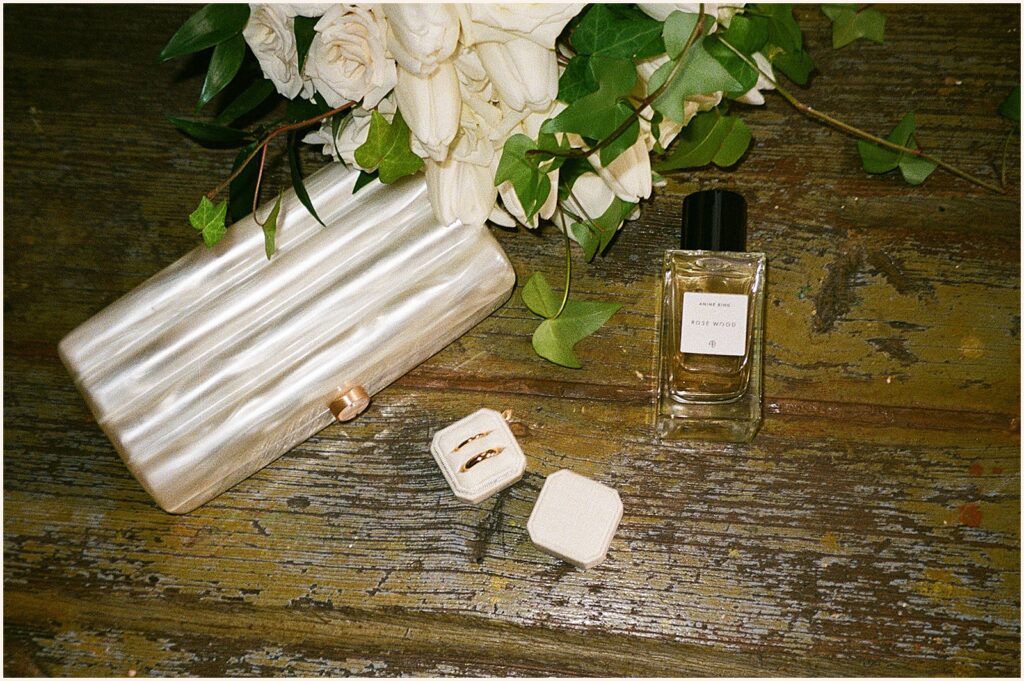 A wedding purse and perfume sit on a wood table in a film wedding photo.