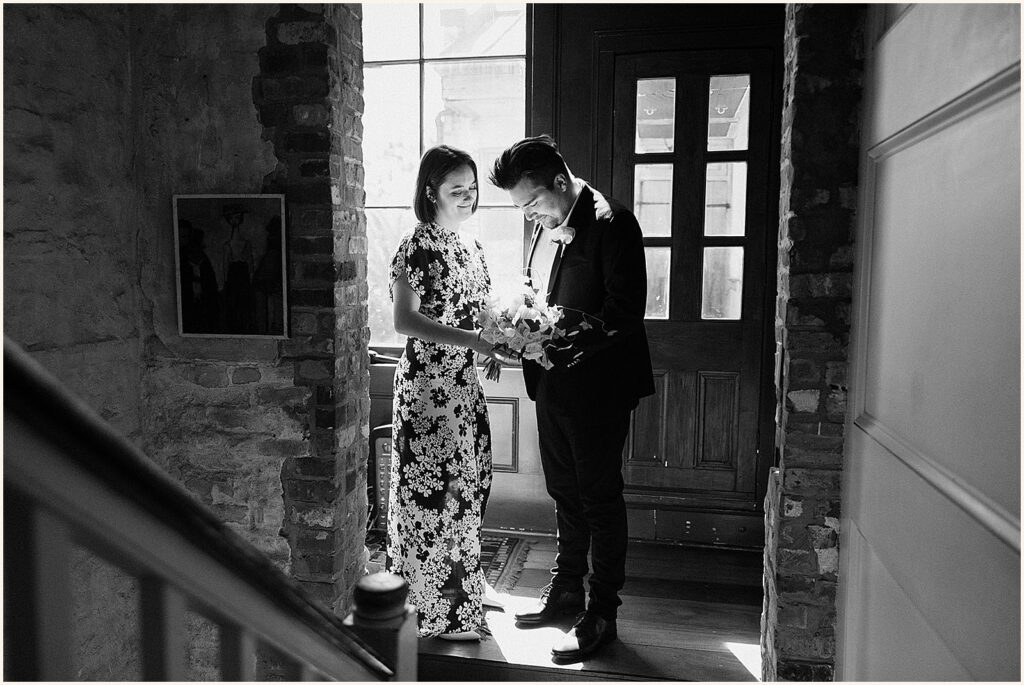 A bride and groom stand in a patch of sun at the bottom of a staircase in a New Orleans wedding venue.