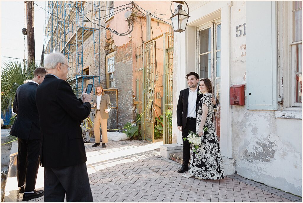 A bride and groom pose for a relative taking a phone photo.