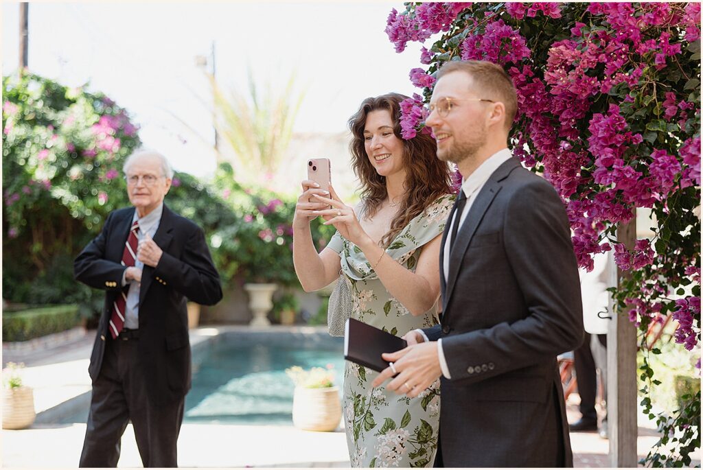 Wedding guests smile and take phone photos.