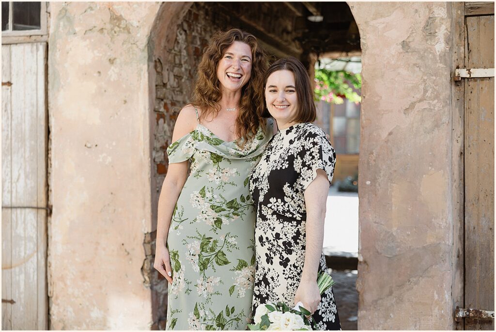 A bride poses with another woman beneath an arch at a New Orleans elopement.