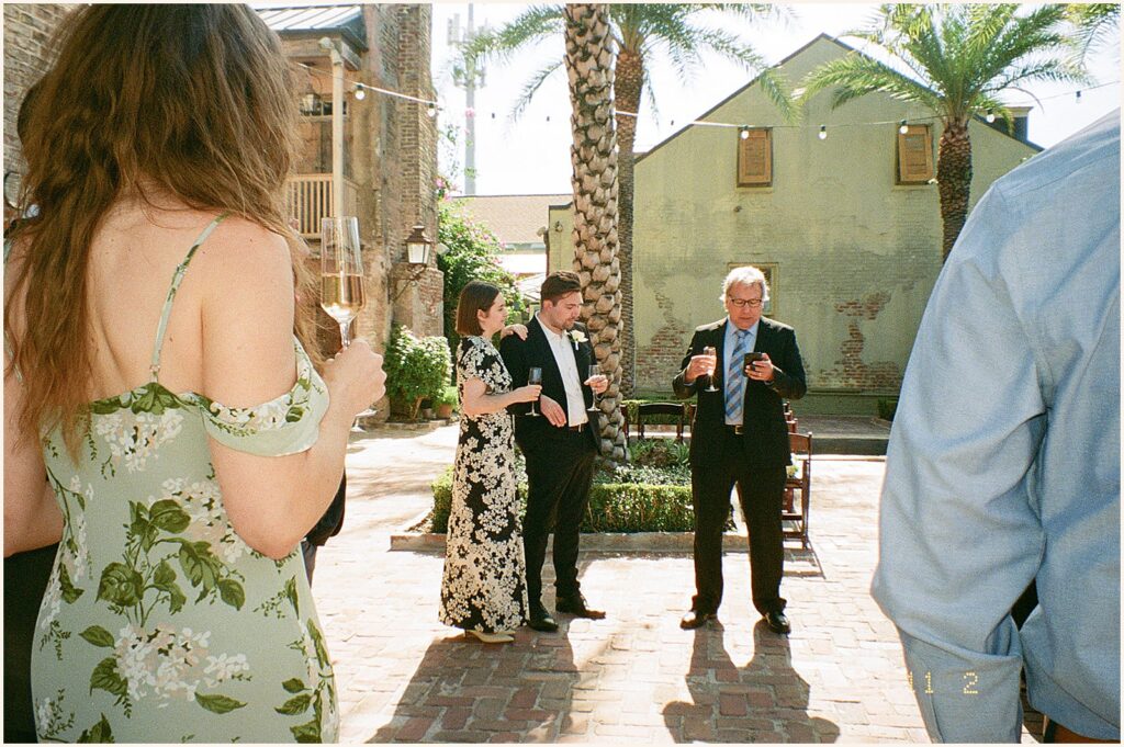 A bride and groom stand beside an older man giving a wedding toast in a film photo.