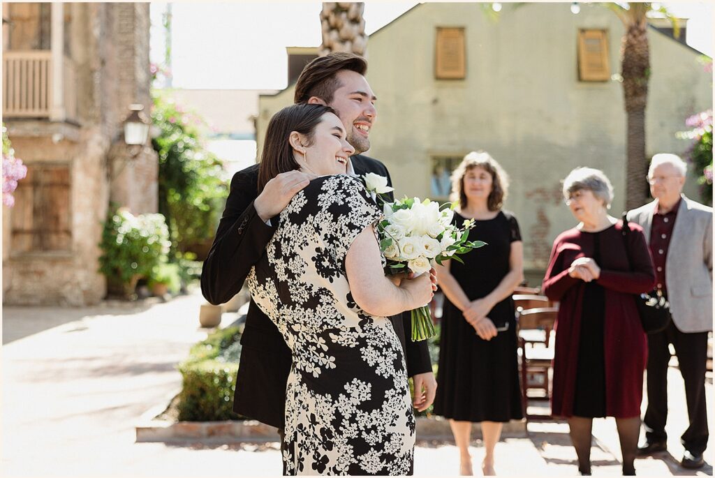 A bride leans on a groom to listen to a speech at their New Orleans elopement.