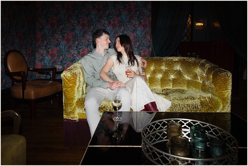 A man and woman sit on a couch smiling for New Orleans engagmeent photos.