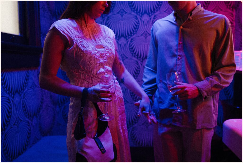A man and woman hold hands in the blue light of a bar.