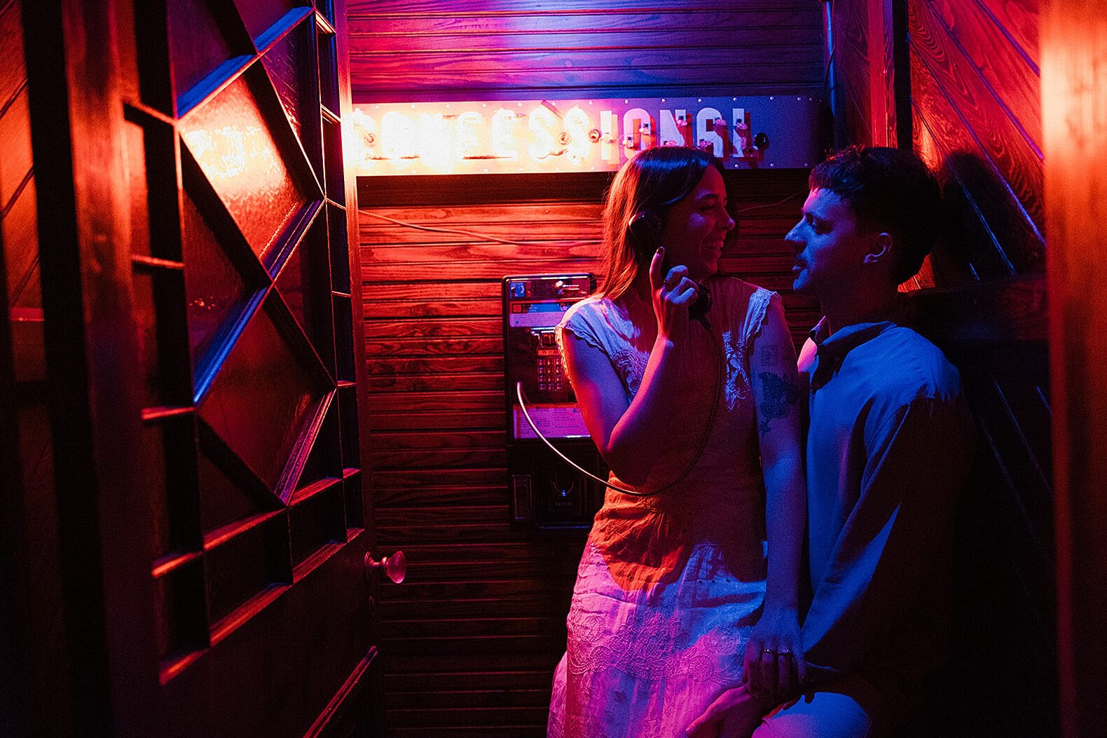 A woman sits on a man's lap in a vintage photo booth in New Orleans engagement photos.
